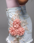 Lichtblauwe korte denim short met een damaged look en bloemenbroderie aan de zijkanten, perfect voor een casual zomerse outfit.