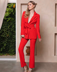 Stijlvol rood damespak met blazer met strikceintuur en bijpassende pantalon, perfect voor een zakelijke look.