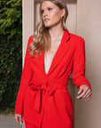 Stijlvol rood damespak met blazer met strikceintuur en bijpassende pantalon, perfect voor een zakelijke look.