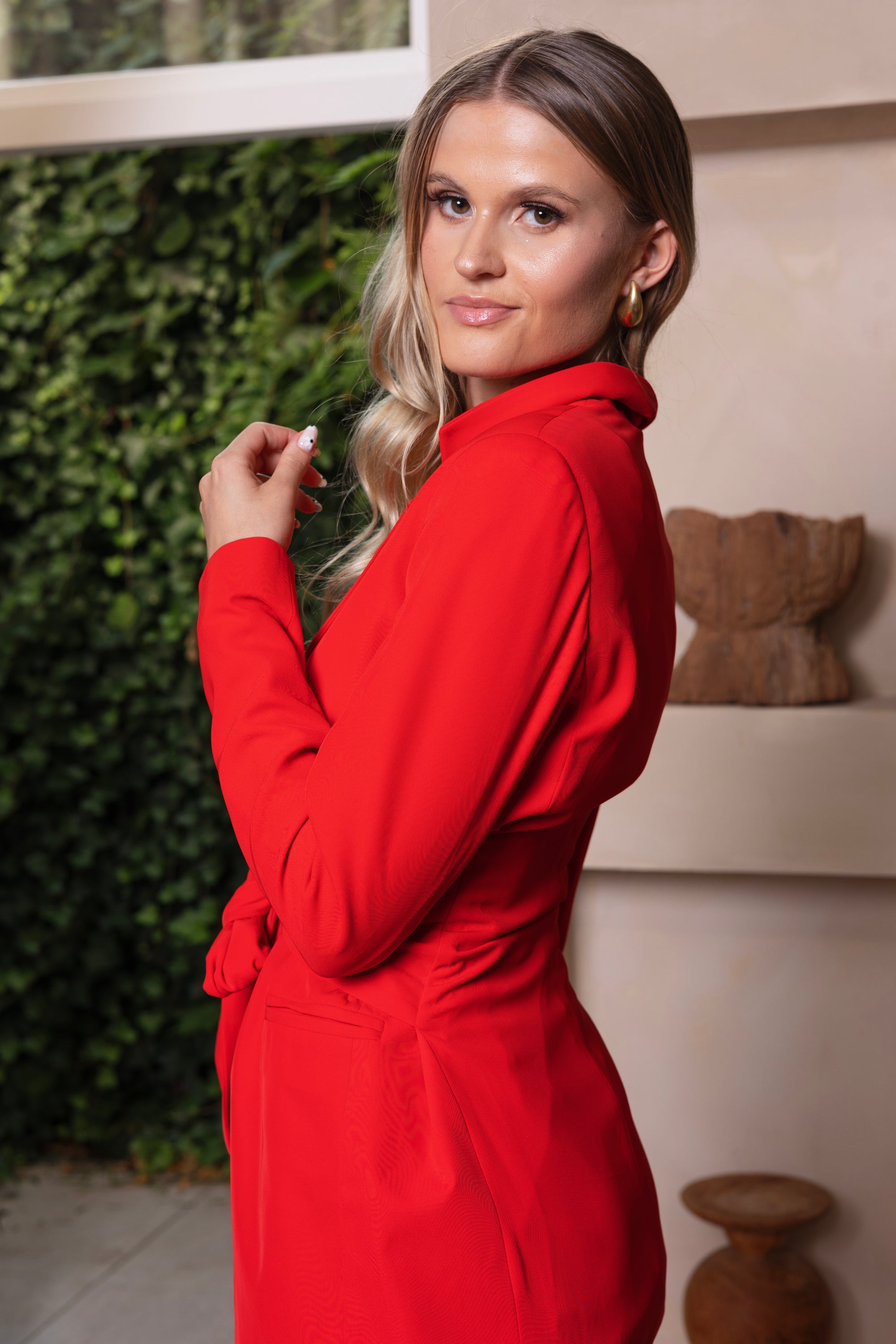 Stijlvol rood damespak met blazer met strikceintuur en bijpassende pantalon, perfect voor een zakelijke look.