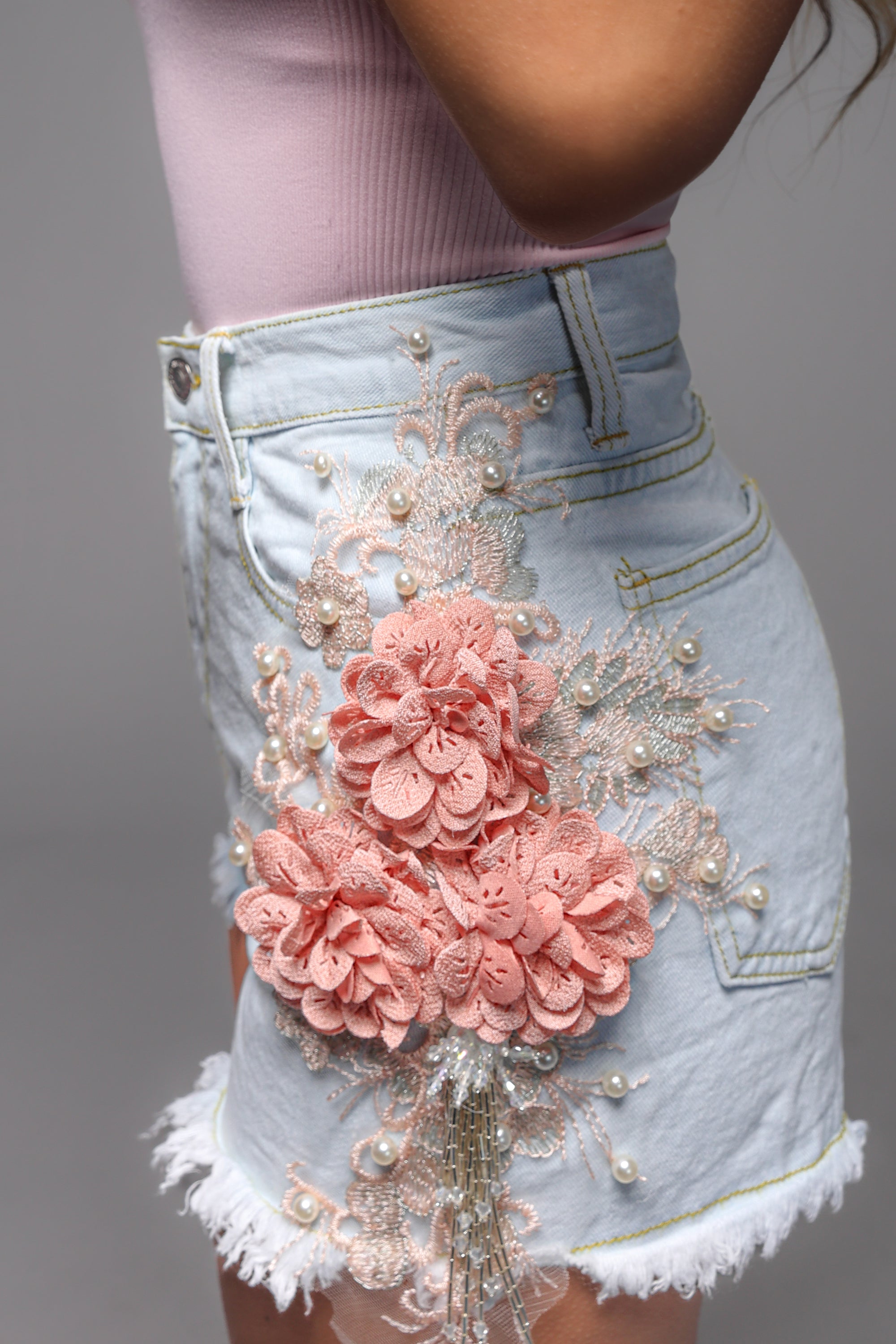 Lichtblauwe korte denim short met een damaged look en bloemenbroderie aan de zijkanten, perfect voor een casual zomerse outfit.