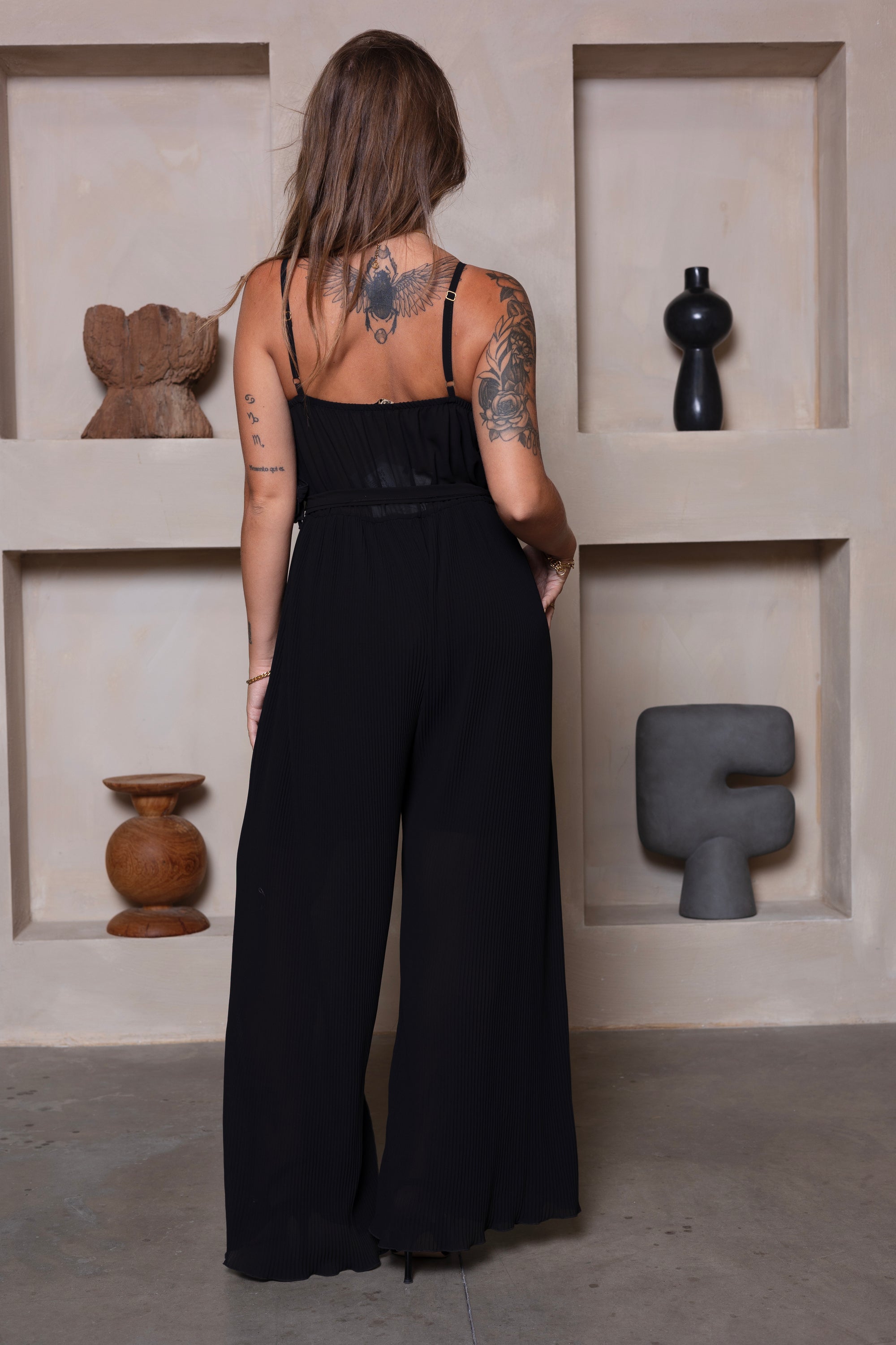 Zwarte lange jumpsuit met strik, spaghettibandjes en wijde pijpen. 